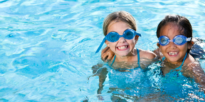 2 young girls with eye goggles in a swimming pool.