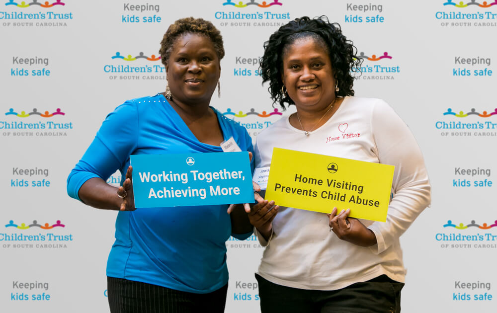 Attendees-pose-with-signs-in-front-of-Childrens-Trust-banner