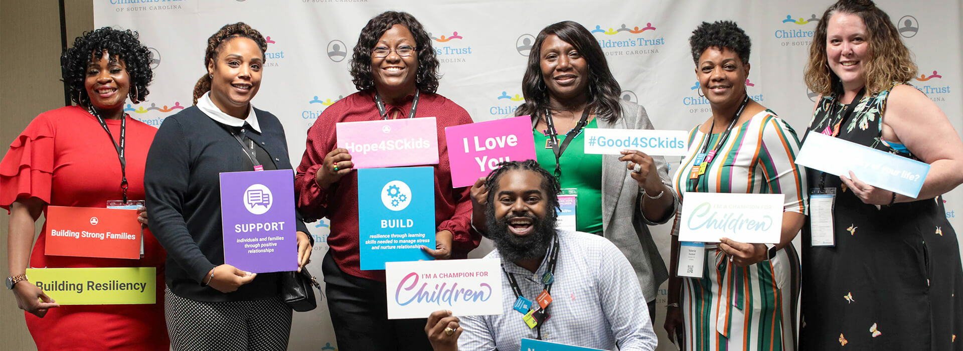 Building Hope for Children Conference attendees pose in front of a step and repeat banner holding signs with positive messages.