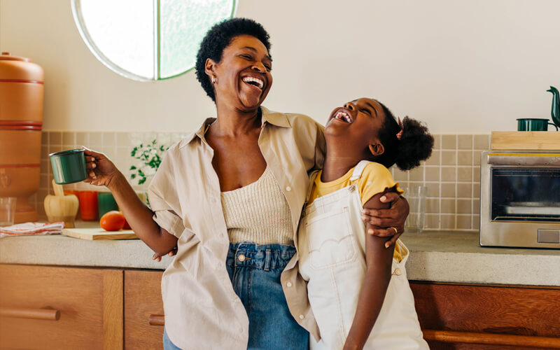 Mother laughing with daughter while embracing her in the kitchen.