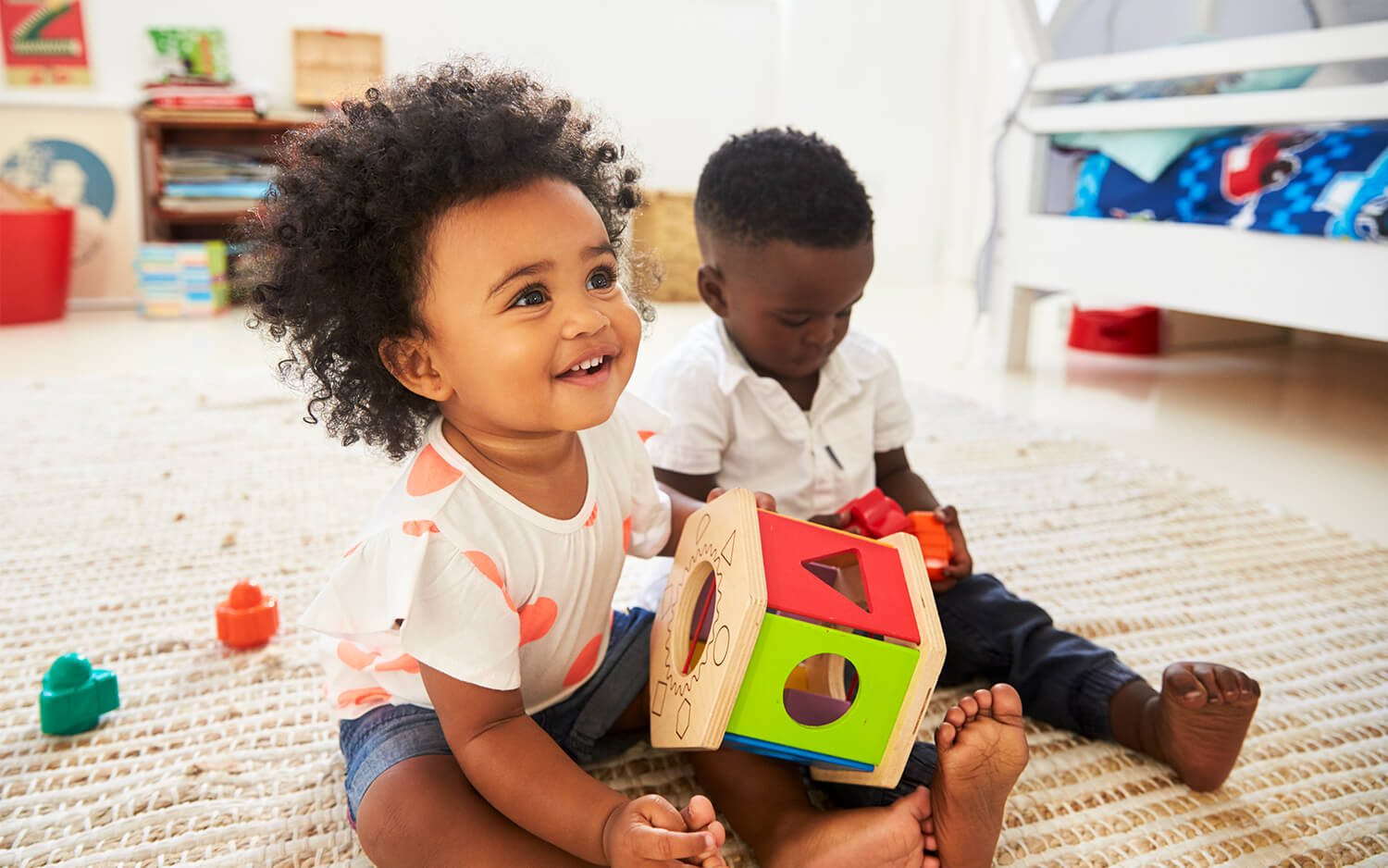 Baby boy and girl playing with toys in playroom together.