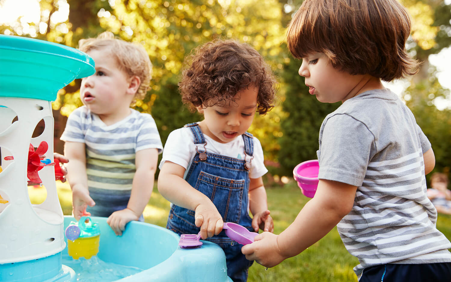 Group of young children playing with water table in the garden.