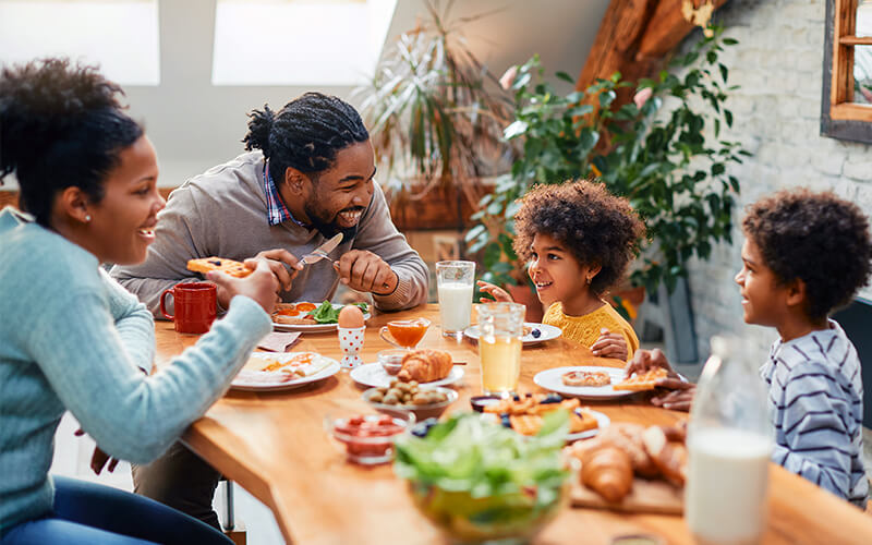 Happy African American family enjoying in conversation while eating breakfast together at dining table