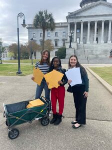 Brooke Ryan, Faith James and Kenzie Russeau stand in front of the SC State House with packets of the Children's Trust legislative agenda