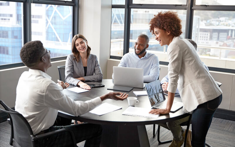 Black businesswoman stands listening to corporate colleagues at a meeting.