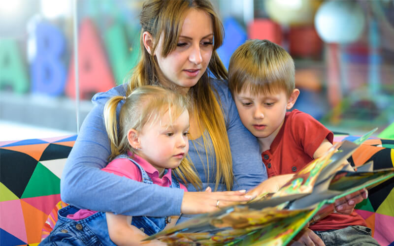 Mother reading large picture book to kids