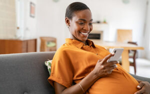 Smiling pregnant adult black woman looking at her mobile phone